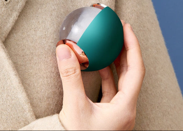 Hand holding a lint roller ball against a beige coat and blue background