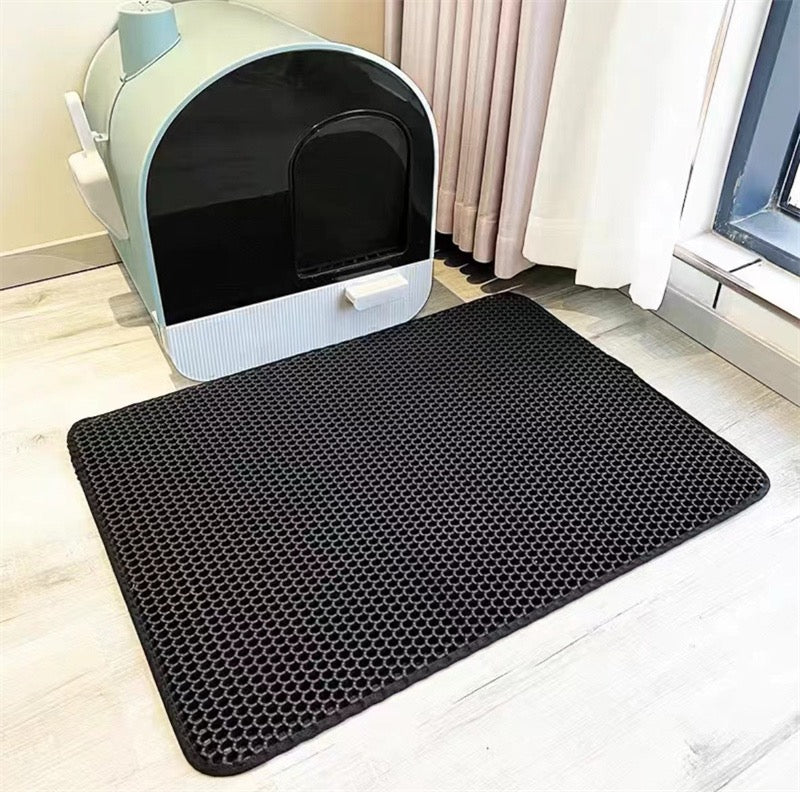 Black hexagonal mat in front of a cat litter box on a light wood floor.
