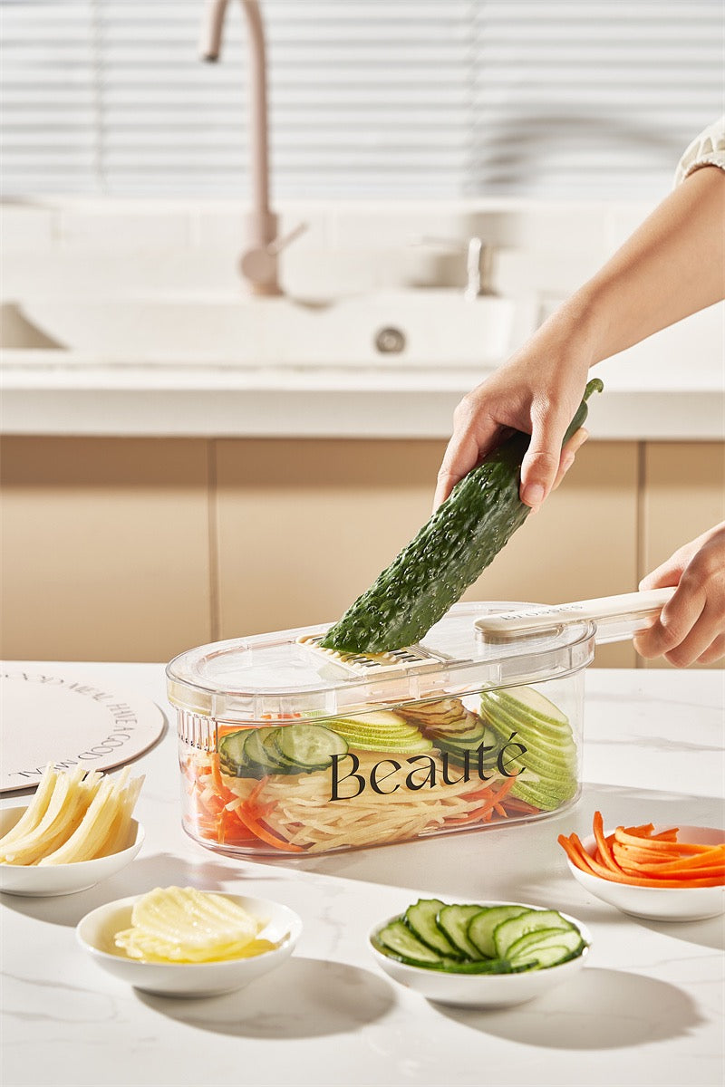 Person using a vegetable peeler to slice a cucumber over a container labeled 'Beaute' in a kitchen setting.