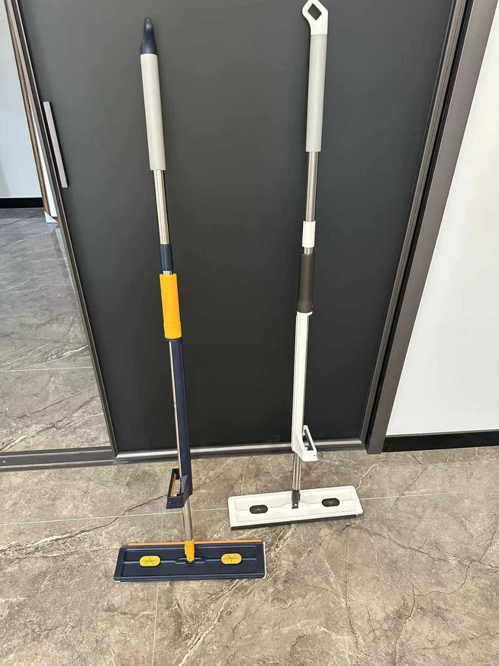 Two Large Flat Mops set against a dark wall on a tiled floor.